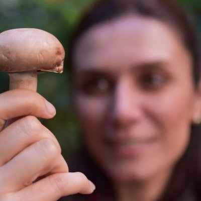 A woman, who's face is out of focus, holds a mushroom head towards the camera